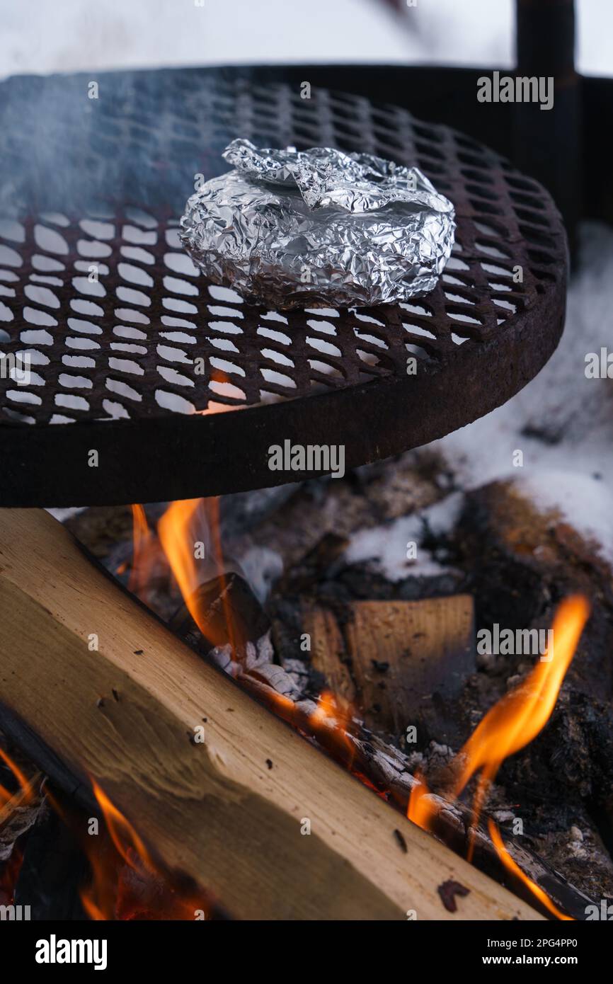 In Folie verpackte Speisen auf einem Grill über dem Lagerfeuer im Winter. Stockfoto