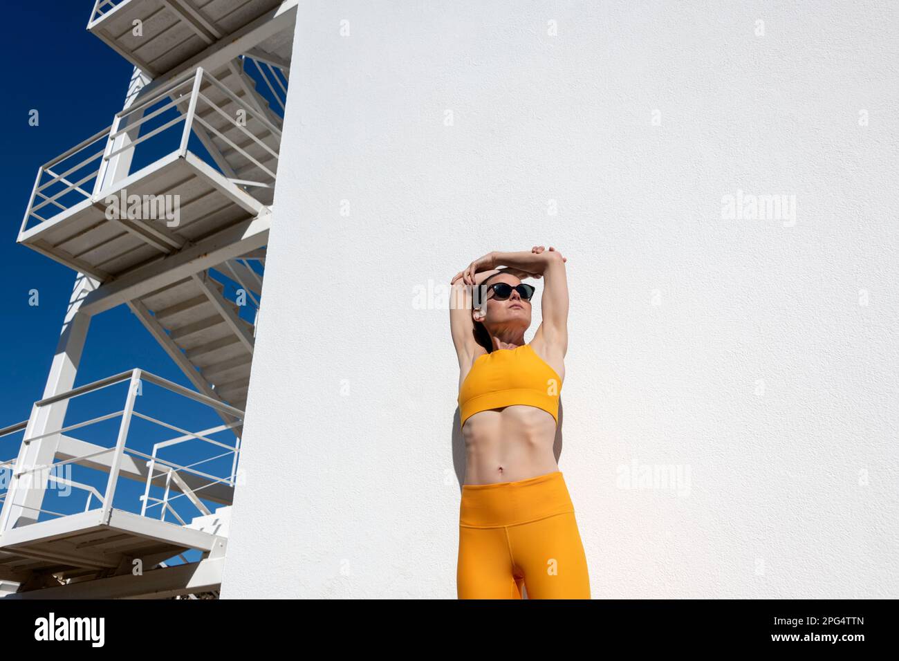Sportliche Frau, die sich draußen in der Sonne mit Armdehnung aufwärmt Stockfoto