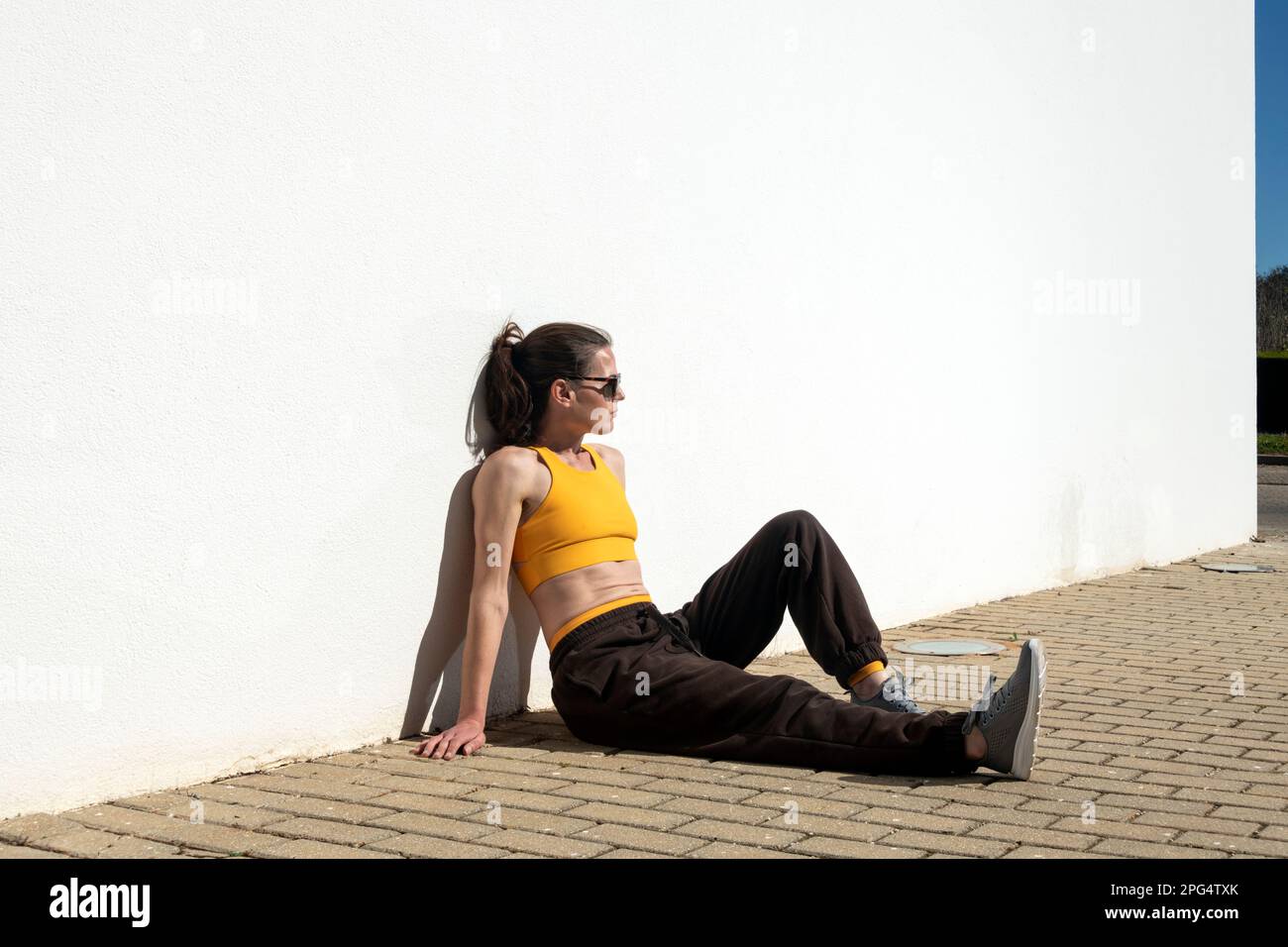 Sportliche Frau, die eine Pause vom Sport macht, in der Sonne sitzt. Stockfoto