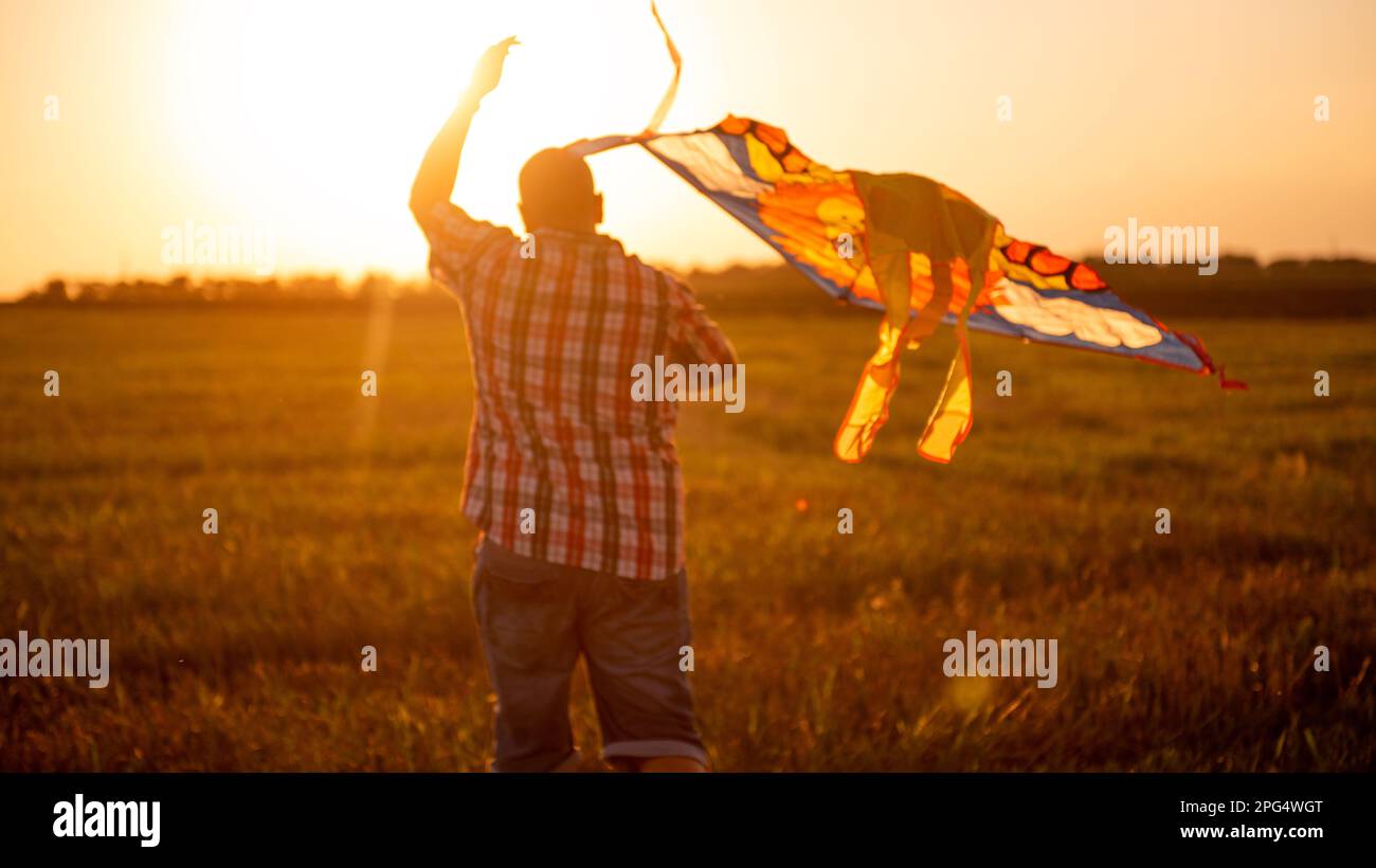 Unscharfer Glatzkopf mit Brille und Drachen im Sonnenfeld des Sonnenuntergangs. Vater spielt mit Kindern in ländlichen Gegenden. Blick durch die Ohren des Mets Stockfoto