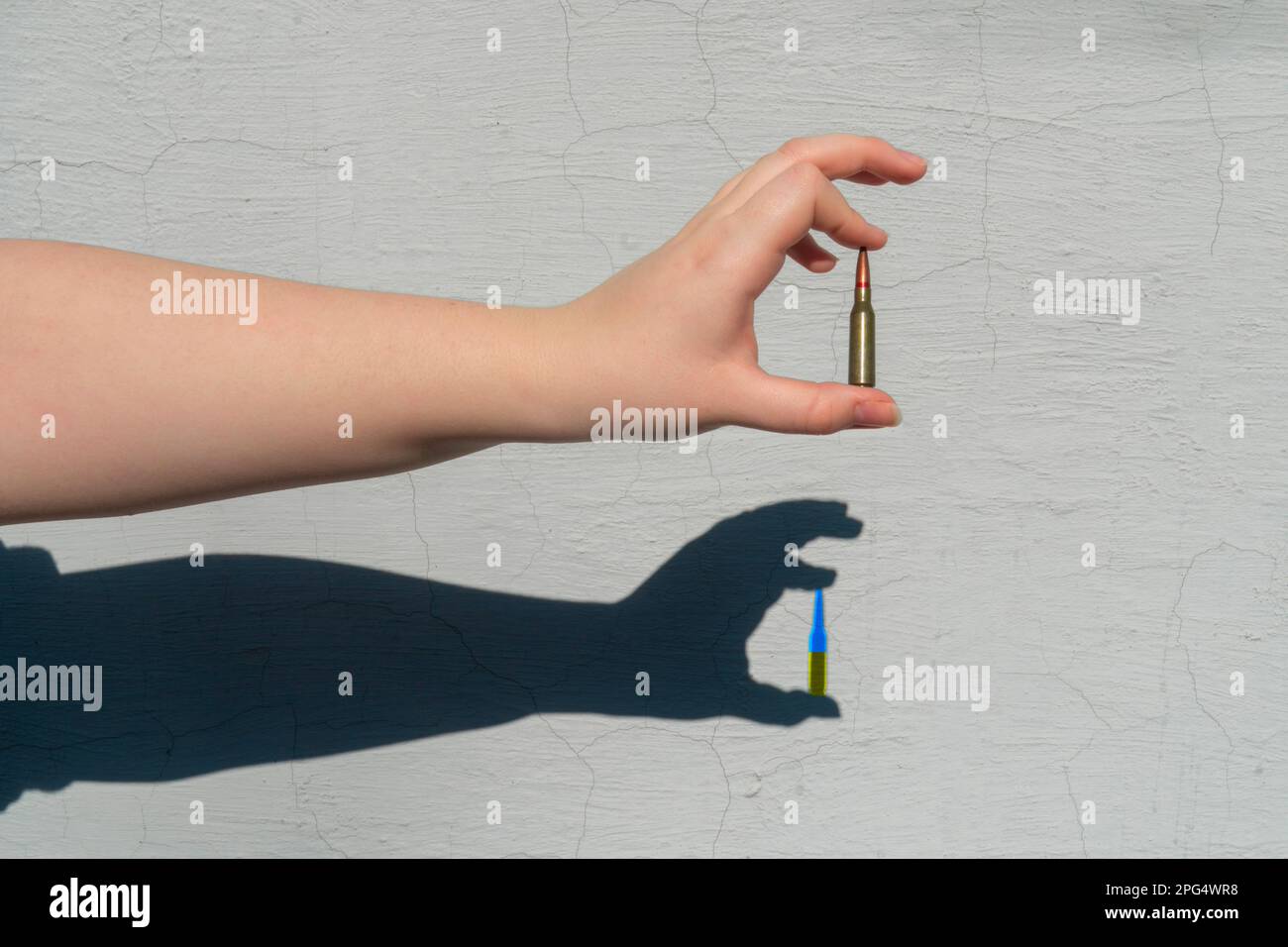 Gewehrpatrone in der Hand. Handschatten an der Wand. Der Schatten der Patrone hat eine gelb-blaue Farbe. Konzept der militärischen Unterstützung für die Ukraine Stockfoto