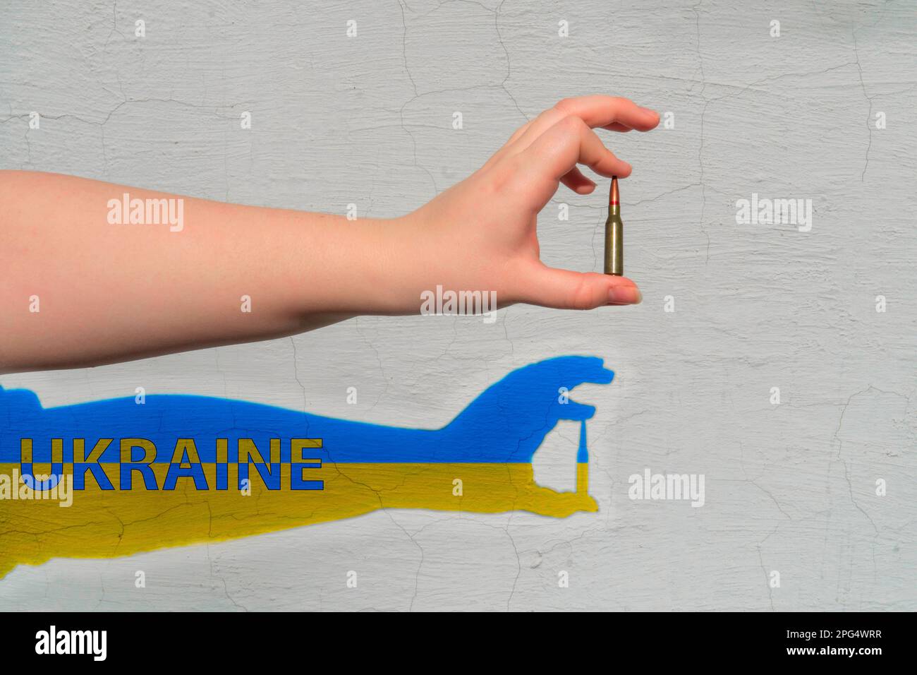 Gewehrpatrone in der Hand. Schatten von gelb-blauer Farbe mit der Inschrift - Ukraine ist an der Wand geformt. Das Konzept der militärischen Unterstützung für die Ukraine Stockfoto