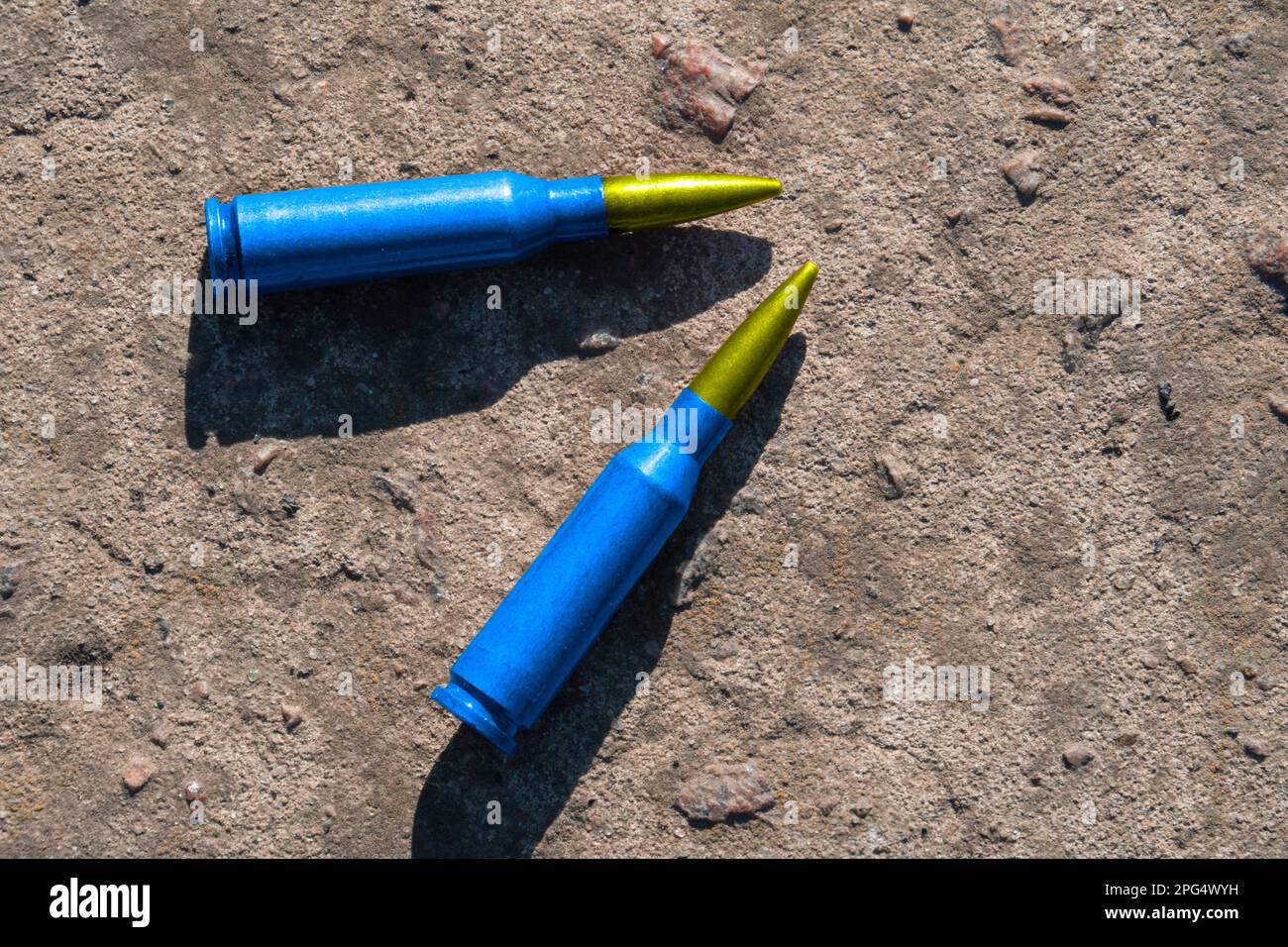 Zwei gelb-blaue Gewehrpatronen (das nationale Symbol der Ukraine) liegen auf einer Betonoberfläche (Nahaufnahme). Das Konzept der militärischen Unterstützung für die Ukraine Stockfoto