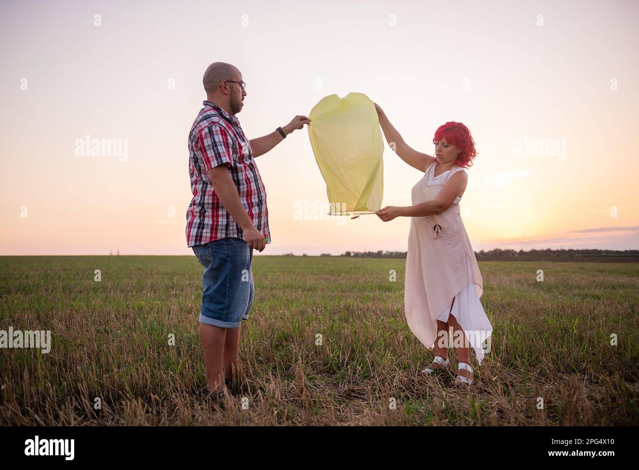 Vielfalt Paar helle gelbe Papierlaterne am Himmel bei Sonnenuntergang auf einem Feld. Beziehung zwischen Mann und Frau. Teamarbeit. Wünsche machen. Konzept von h Stockfoto