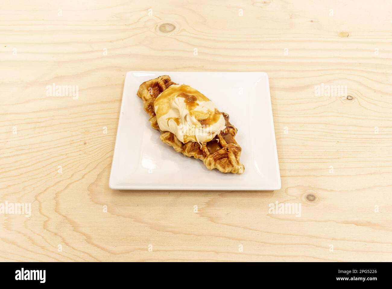 Ein frisch gebackenes Croissant mit Sahne und Dulce de leche Sirup auf einem unlackierten Holztisch Stockfoto