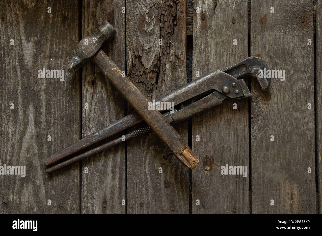 Alter rostiger Gasschlüssel und Hammer liegen auf einem Holztisch in Nahaufnahme Stockfoto