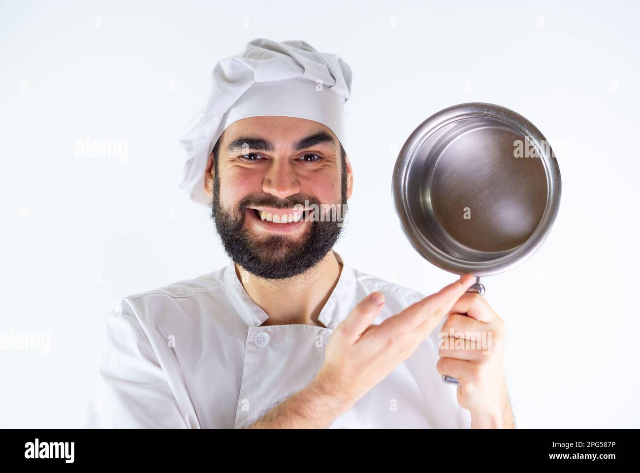 Der junge Koch zeigt einen Edelstahltopf, während er lächelt und in die Kamera schaut. Isoliert auf weißem Hintergrund Stockfoto