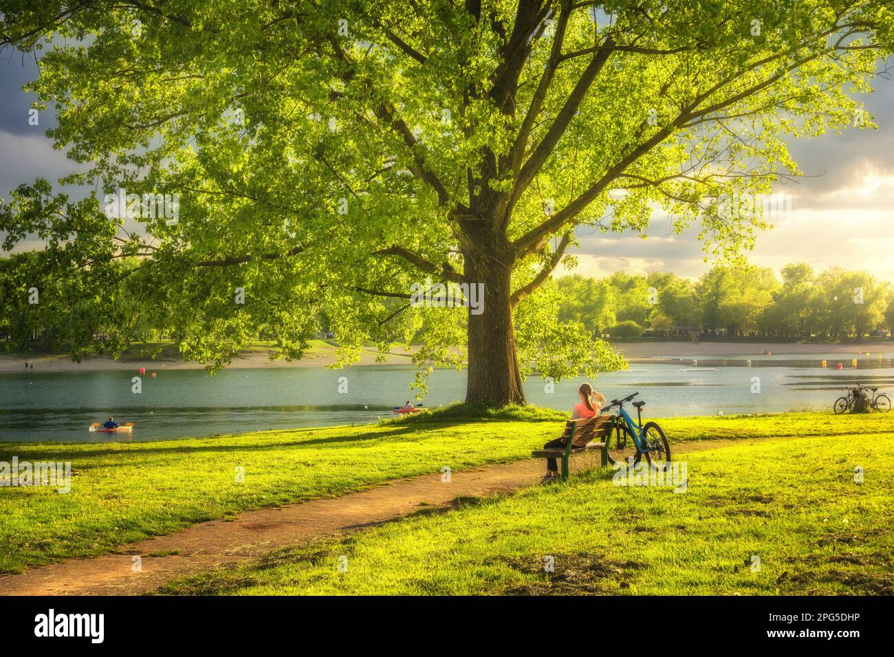 Frau sitzt auf Bank und Mountainbike, grüne Bäume Stockfoto