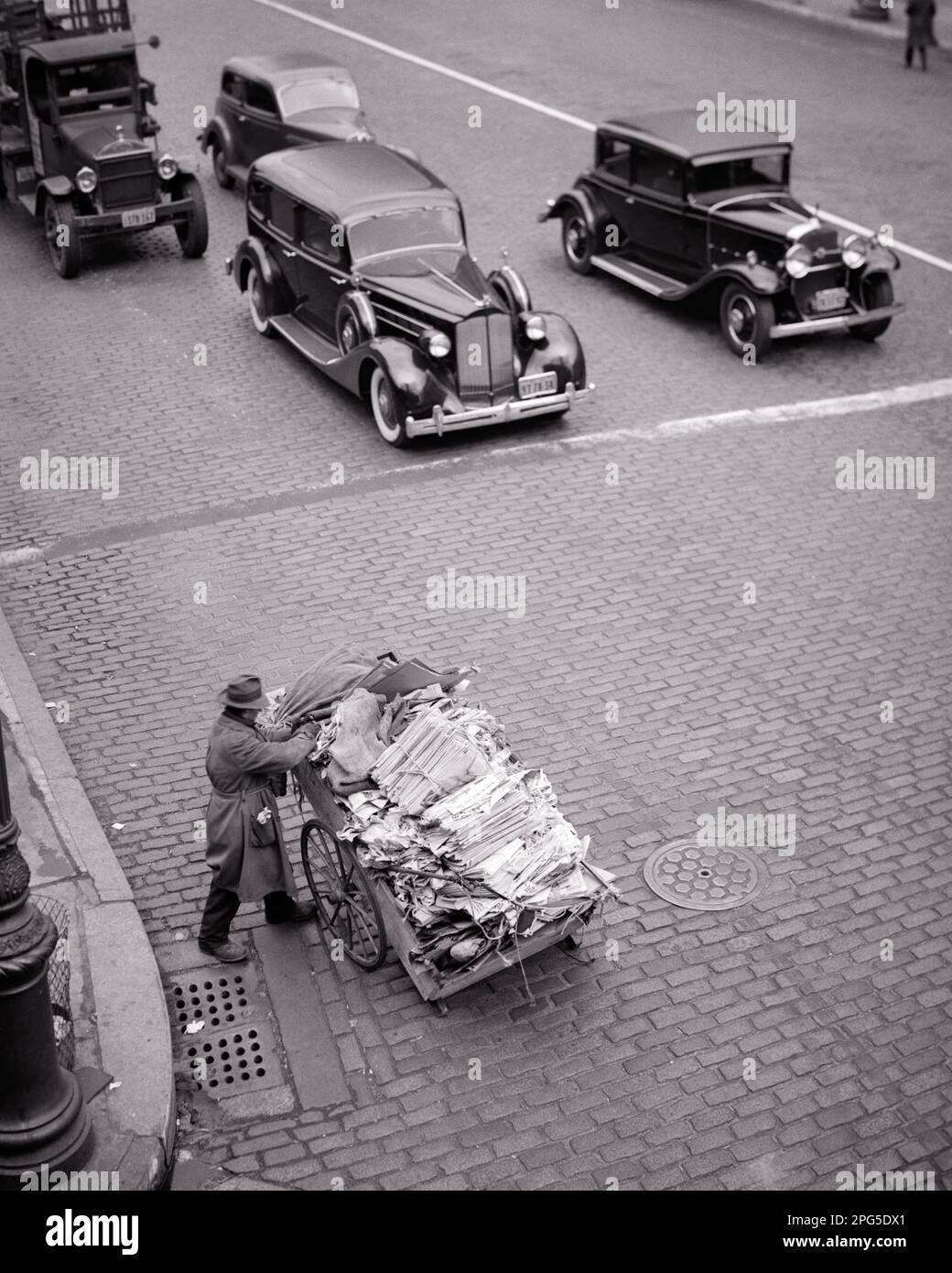 1930S JUNKMAN MIT ZWEIRÄDRIGEM WAGEN, DER ZEITUNGEN SAMMELT, NEBEN DER LUXURIÖSEN LIMOUSINE BROOKLYN NYC USA - Q37712 CPC001 HARS INFORMATIONEN LIFESTYLE GESCHICHTE JOBS LUXUS USA TEXT RAUM VOLLE LÄNGE PERSONEN INSPIRATION VEREINIGTE STAATEN VON AMERIKA AUTO MÄNNER ZEITUNGEN BERUF NY TRANSPORT B&W TRAURIGKEIT BROOKLYN FREIHEIT QUALIFIKATION FÄHIGKEITEN KARTON HOCHWINKEL ENTDECKUNG RECYCLING AUTOS CAREERS CHOICE ARBEITSMÖGLICHKEITEN NYC BERUFE NEW YORK AUTOMOBILE CITY FAHRZEUGE ROLLTEN NEW YORK CITY ZIEGELSTEINPFLASTER UND SAMMELTEN LÖSUNGEN FÜR MITTELERWACHSENE MÄNNER IN SCHWARZ-WEISS Stockfoto