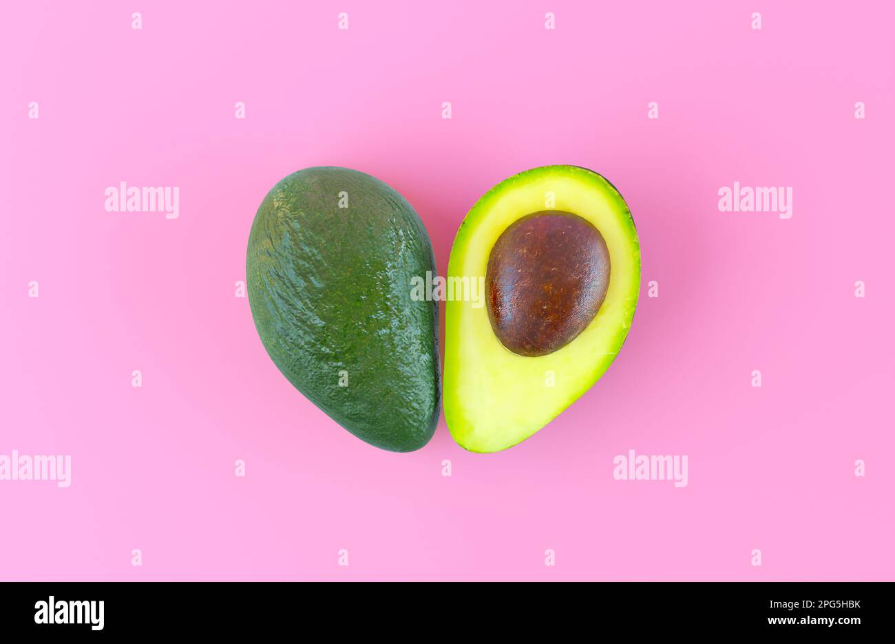 Eine halbe Avocado mit Blick von oben, isoliert auf einem pinkfarbenen, flachen Hintergrund. Reife, köstliche Avocado in Herzform. Das vegane Konzept Stockfoto