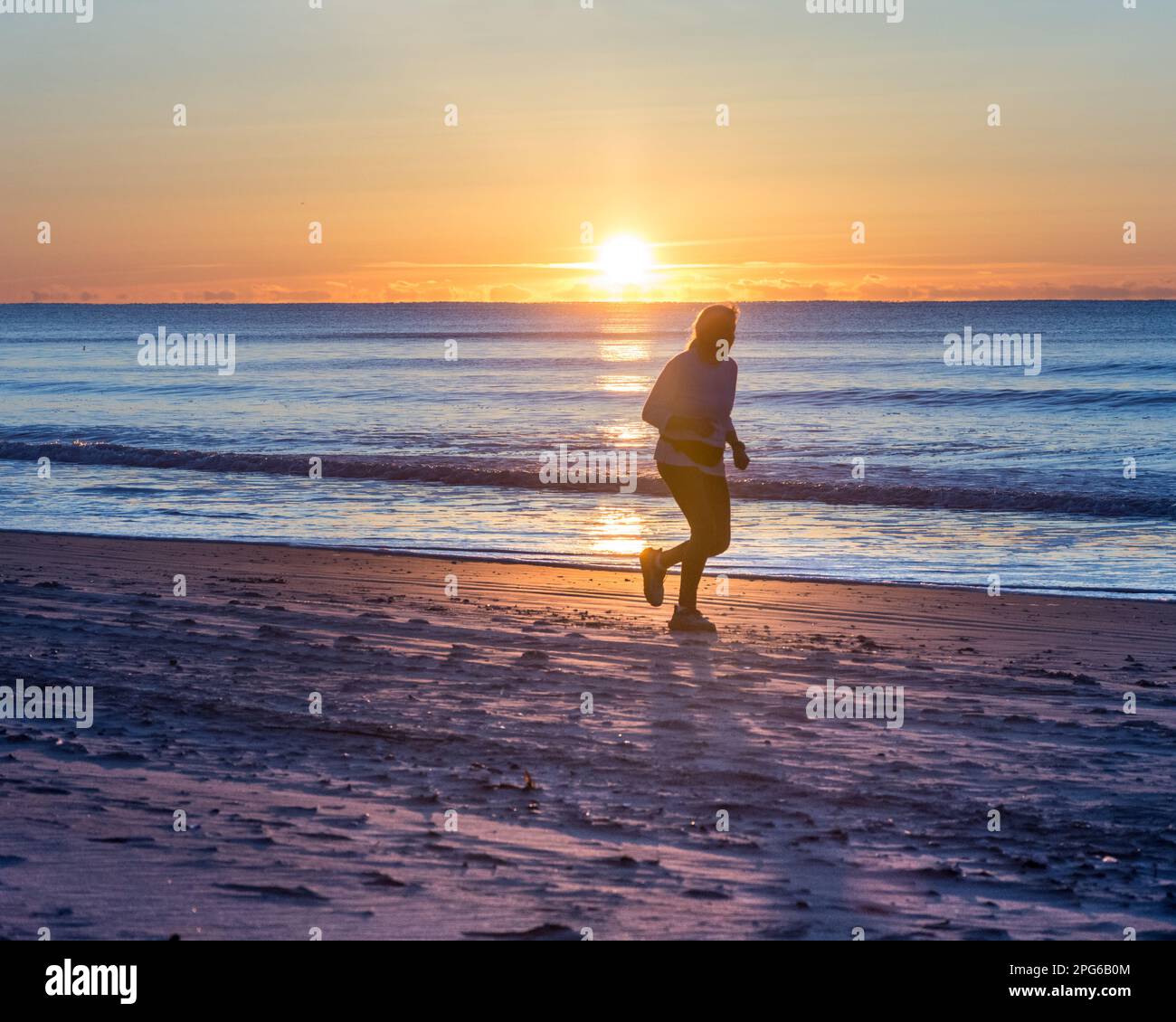 North Myrtle Beach, North Carolina, USA: Einsamer Läufer in Silhouette, der entlang der Küste in Richtung Kamera läuft und die Sonne direkt über dem Horizont aufgeht. Wunderschöner Schachzug Stockfoto