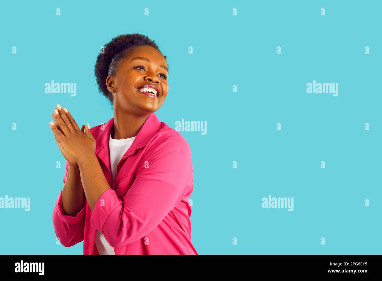Fröhliche lächelnde junge afroamerikanische Frau mit Händen in Gebetsgesten auf blauem Hintergrund. Stockfoto