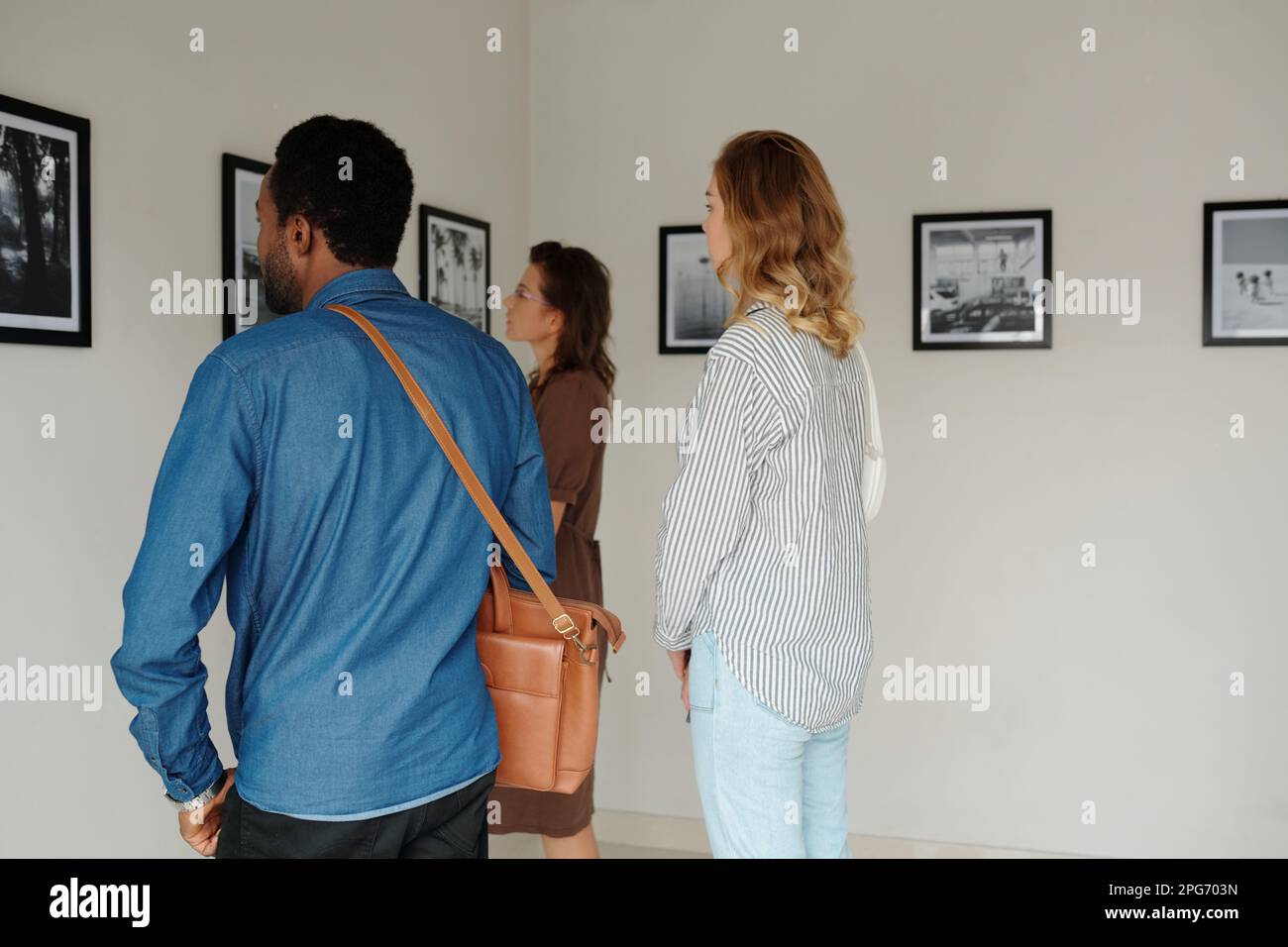 Eine Gruppe interkultureller Studenten oder Gäste in Freizeitkleidung, die vor einer Wand mit Kunstwerken stehen, während sie die Galerie der modernen Künste besuchen Stockfoto