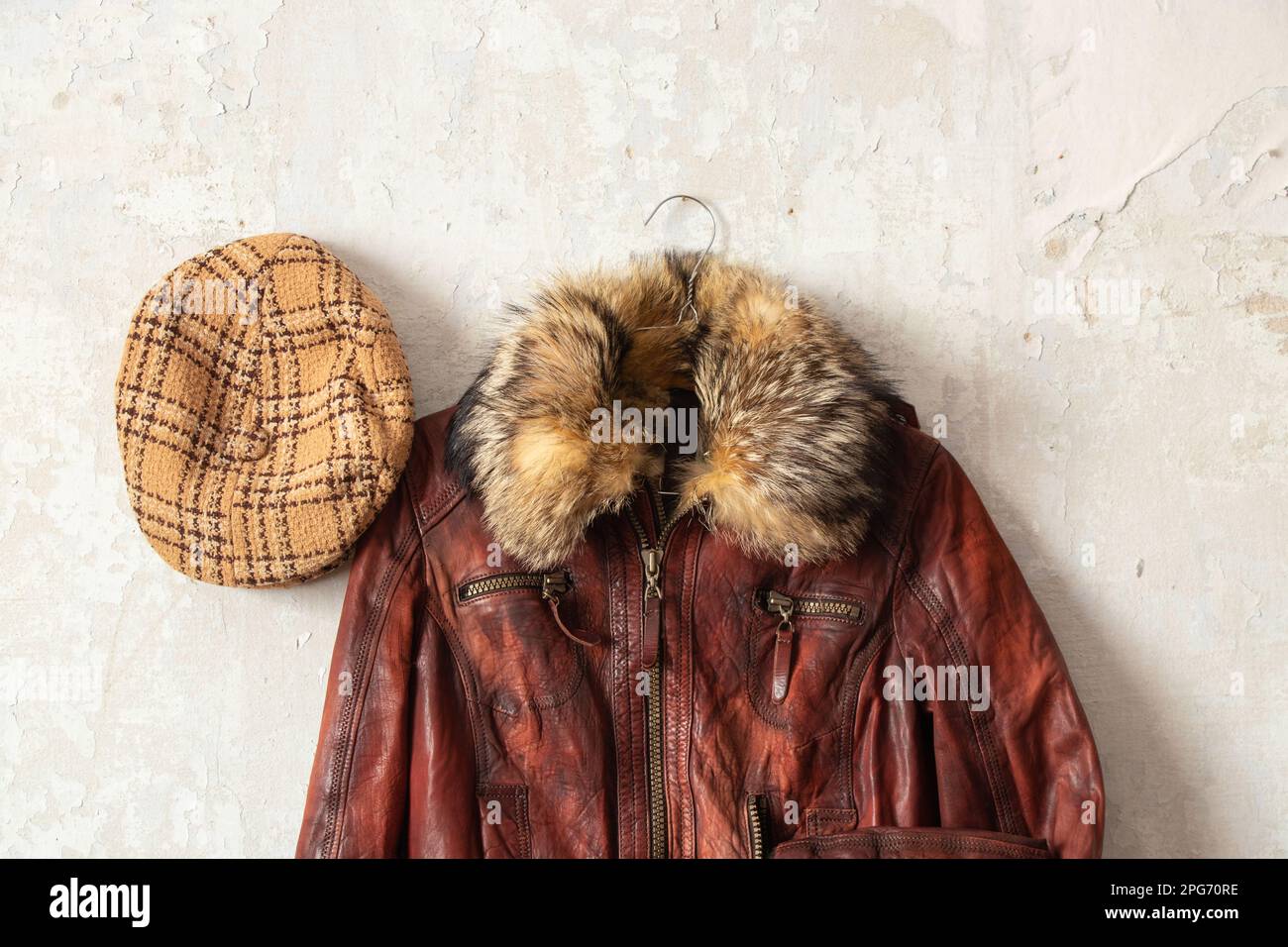 Rote Lederjacke und karierte Mütze, die an der weißen alten Wand hängt, Mode Stockfoto