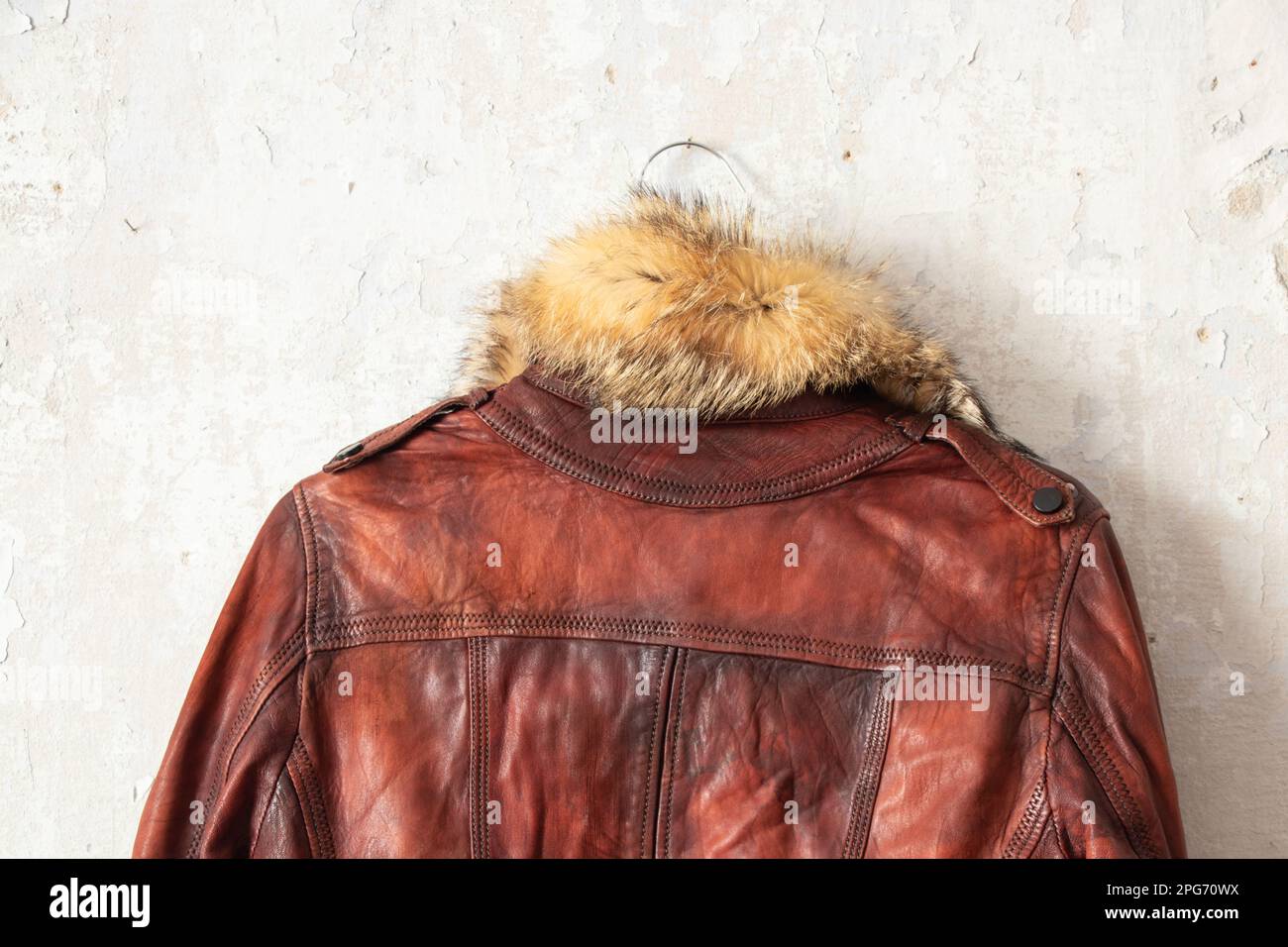 Winterjacke aus rotem Pelzleder, die an einem Kleiderbügel an einer weißen Wand hängt Stockfoto