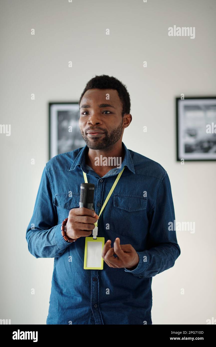 Junger afroamerikanischer Journalist mit Mikrofon, der vor der Kamera steht und während der Eröffnung der Kunstausstellung interviewt wird Stockfoto