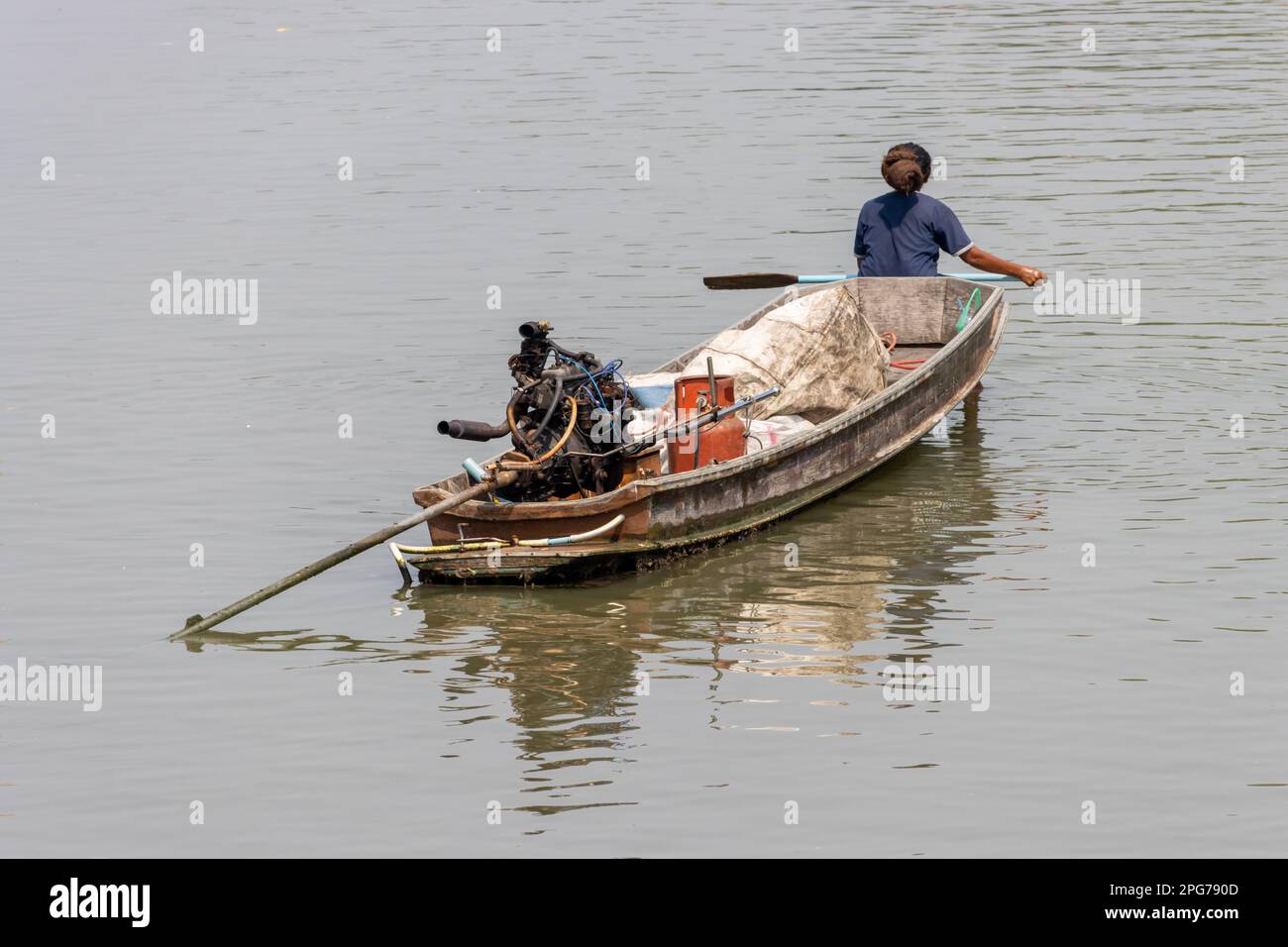 Eine Frau paddelt am Bug eines Schiffes, das recycelbare Güter in Thailand transportiert Stockfoto