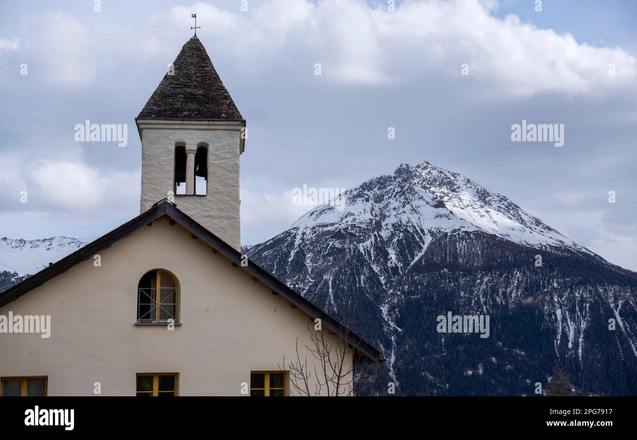Die Kirche in Vnà (1.602 m) mit einem Dreiecksgipfel (wahrscheinlich Piz Ajüz [2.778 m]) dahinter - Unterengadin, Graubünden, Schweiz Stockfoto