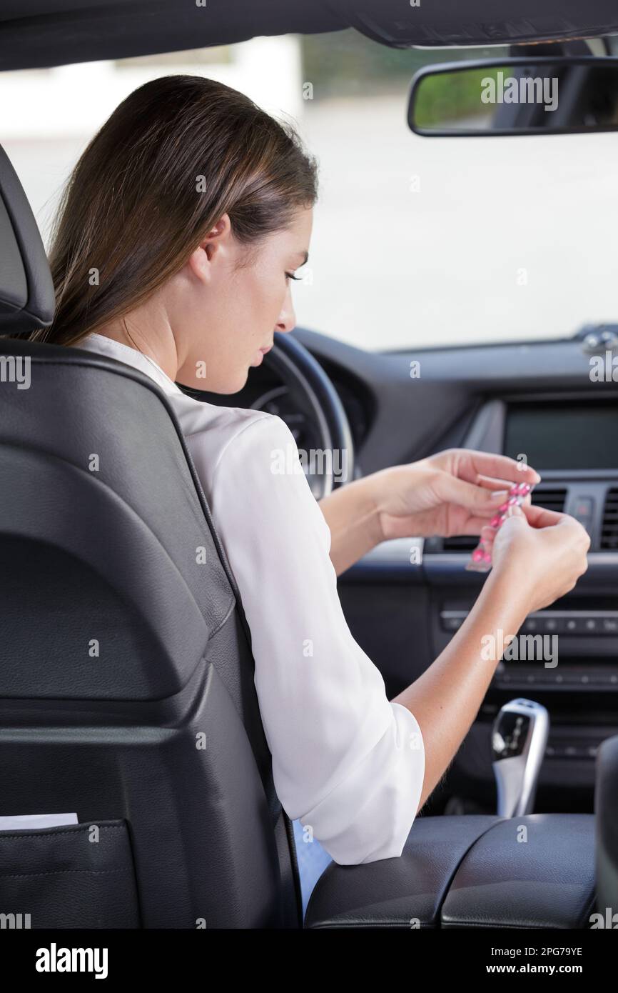 Frauen, die während der Fahrt Pillen in seinem Auto schlucken Stockfoto