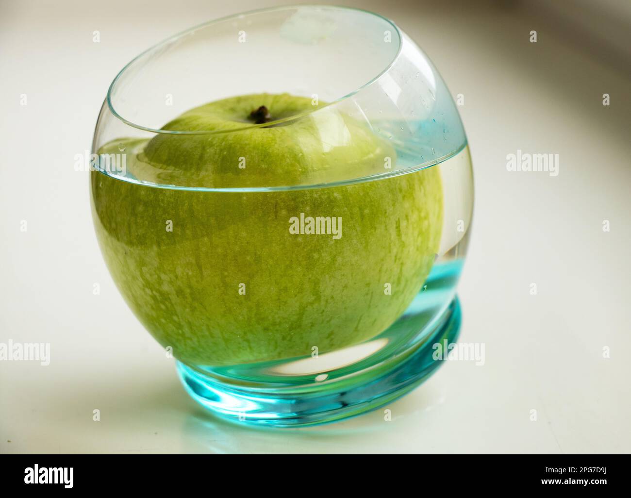 Ein grüner Apfel in einem Glas Wasser auf hellem Hintergrund Stockfoto