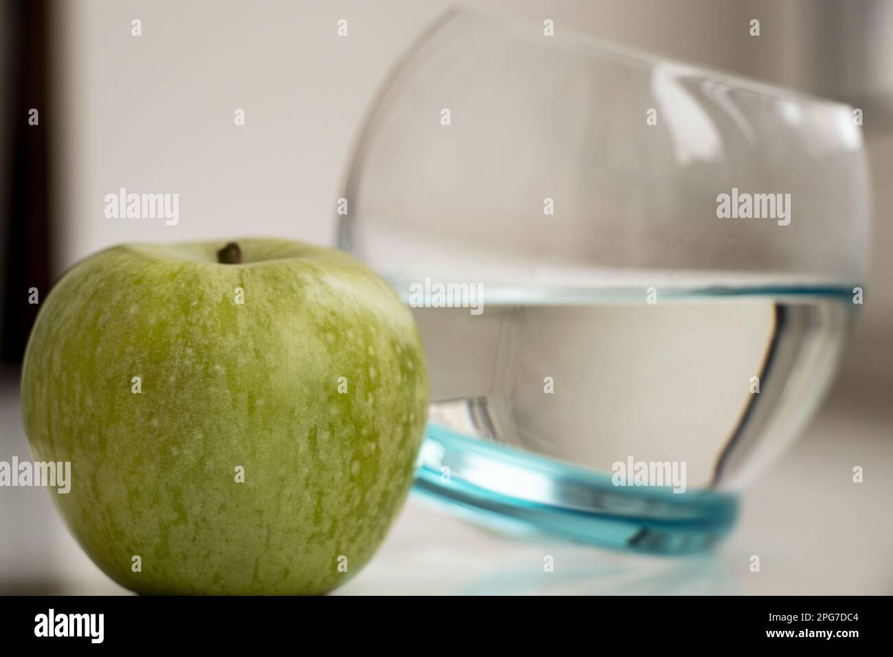 Ein grüner Apfel und ein Glas Wasser daneben auf hellem Hintergrund Stockfoto