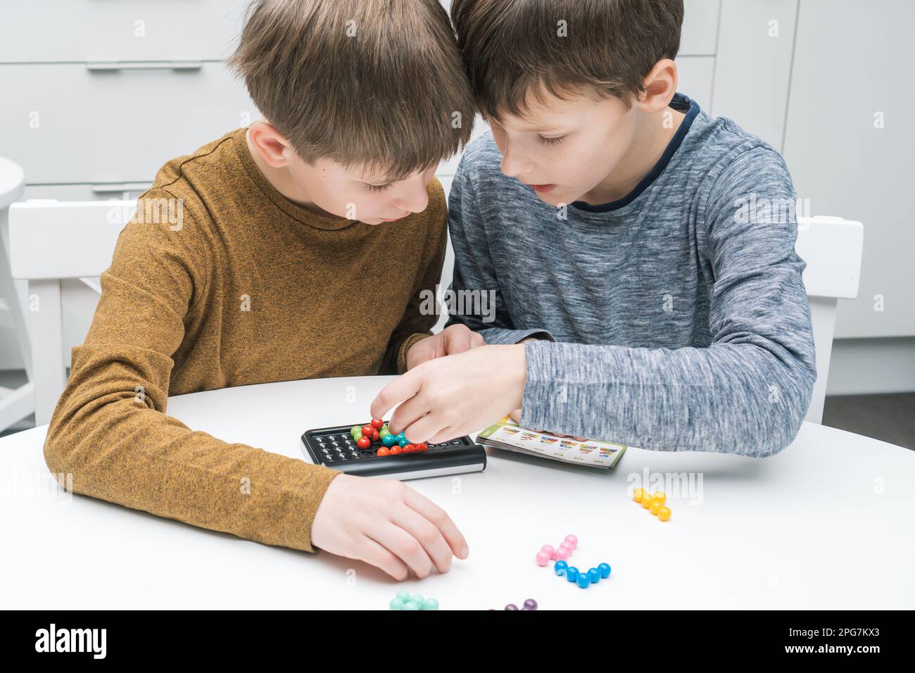Zwei nachdenkliche und begeisterte Jungen spielen pädagogisches Strategiespiel mit Schwarzfeld und bunten Bällen auf dem Tisch. Rätsel lösen und finden Stockfoto