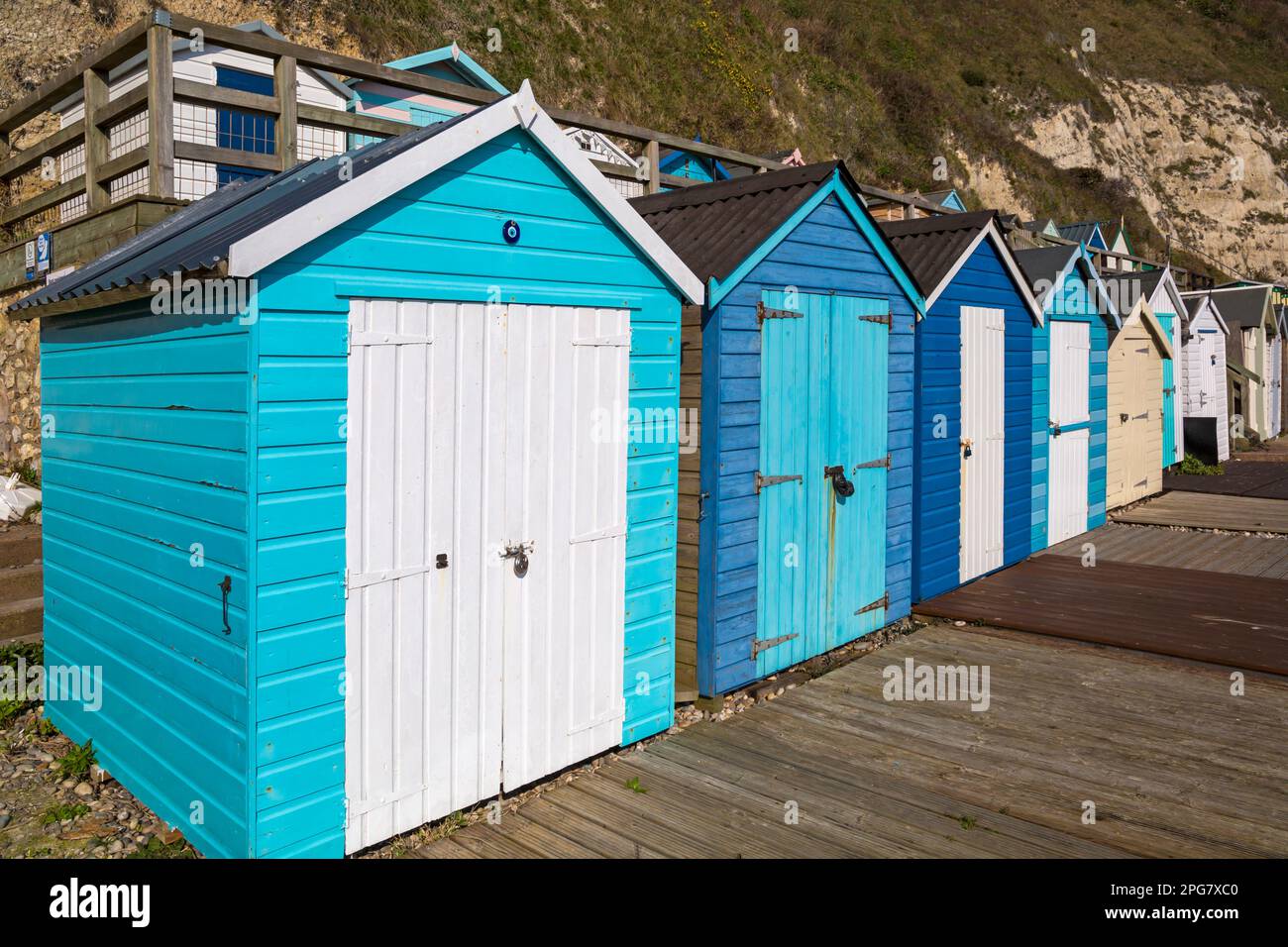 Reihen blauer Strandhütten am Fuß der Klippen am Beer Beach, Seaton, Devon UK im März Stockfoto