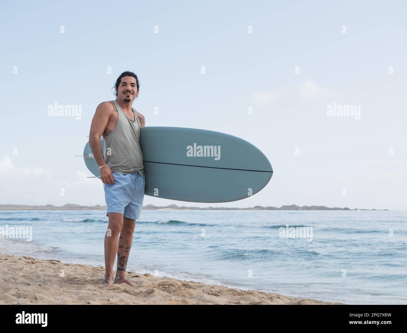 Hispanischer Surfer am Strand mit Surfbrett Stockfoto