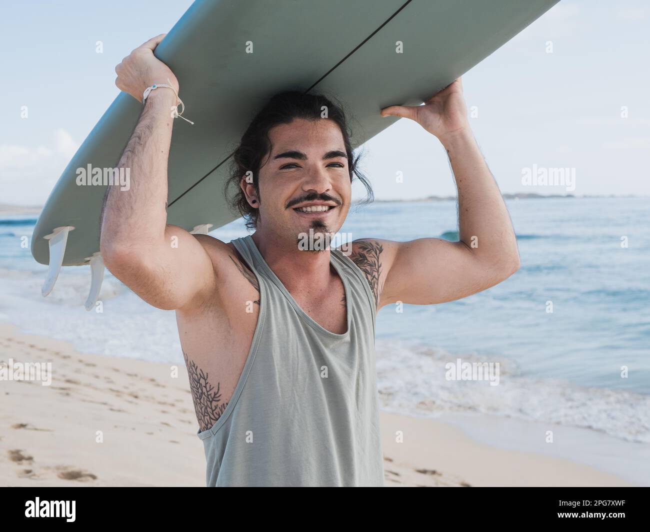 Ein hispanischer Surfer, der am Strand steht und sein Surfbrett hält Stockfoto