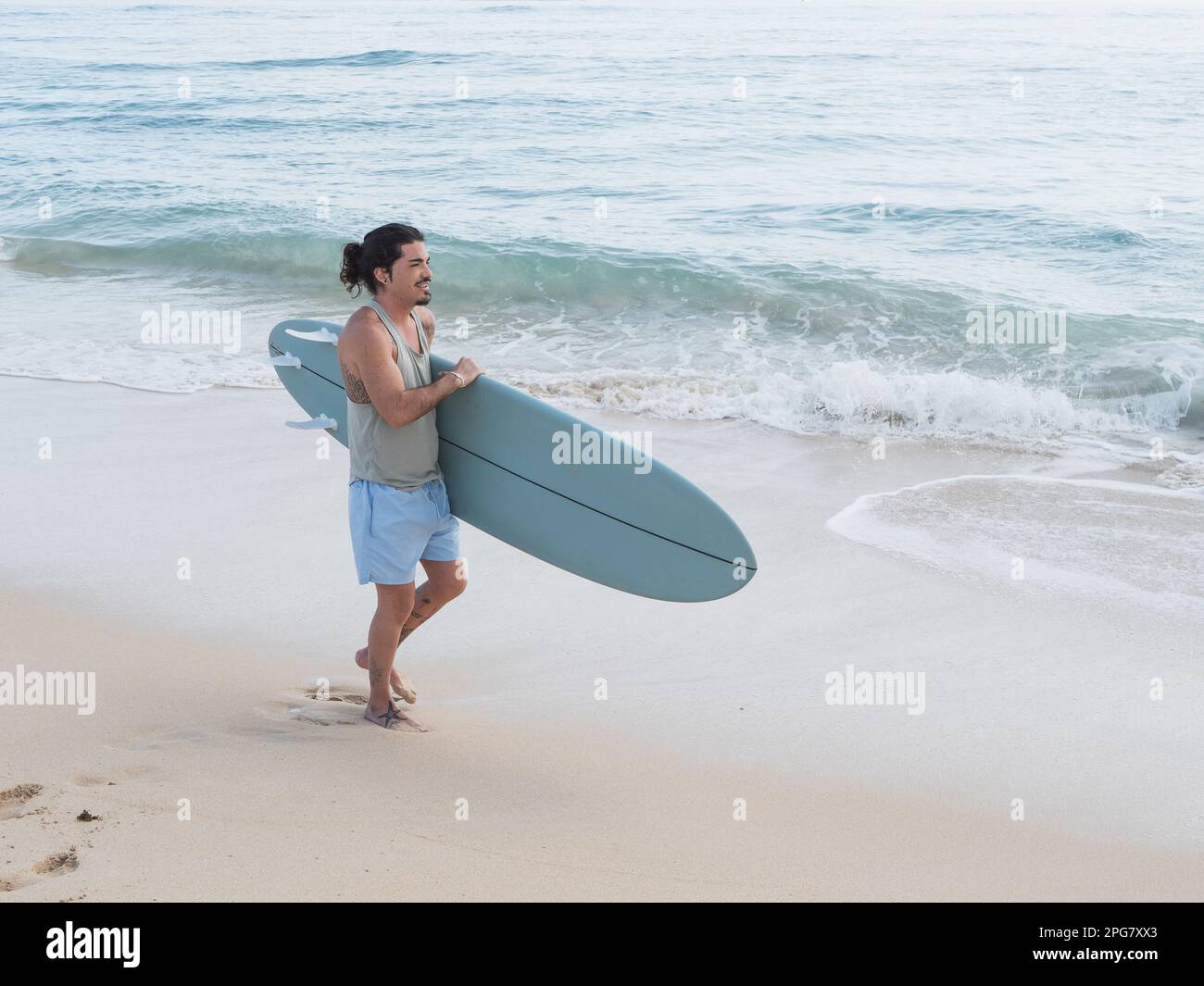 Hispanischer Surfer, der mit seinem Surfbrett am Strand spaziert Stockfoto