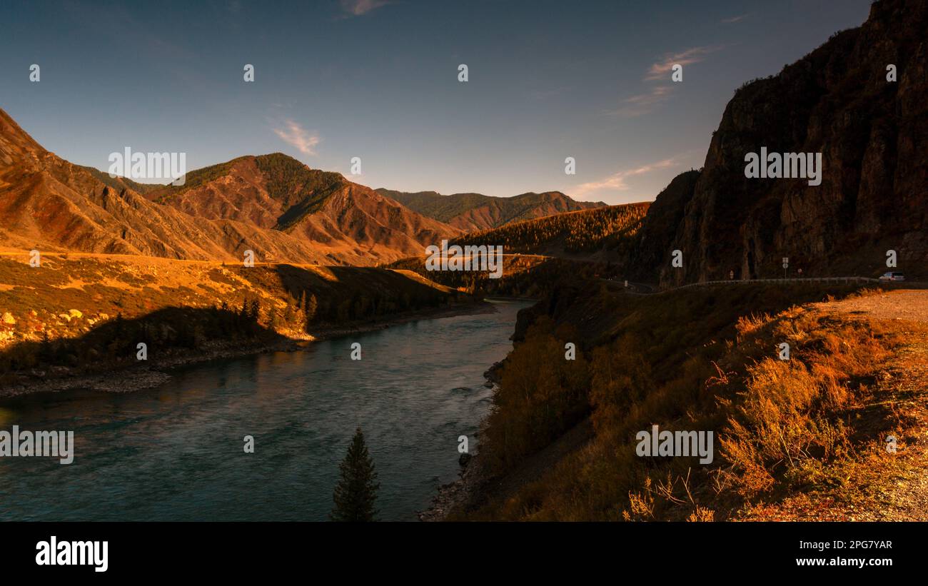 Die Bergstraße Chuisky Trakt führt im Herbst in Sibirien neben dem Katun in Altai unter einem Felsen im Schatten. Stockfoto