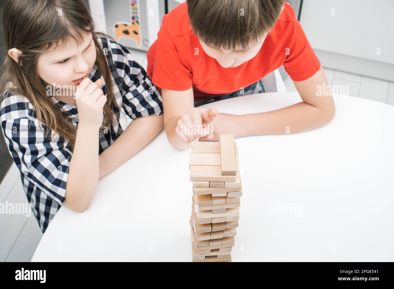 Ernsthafte, konzentrierte Kinder, Junge und Mädchen denken über Strategie beim Brettspiel aus hölzernen Ziegeltürmen nach. Bewegen Sie die Blöcke vorsichtig von den Pyramiden auf dem Tisch Stockfoto