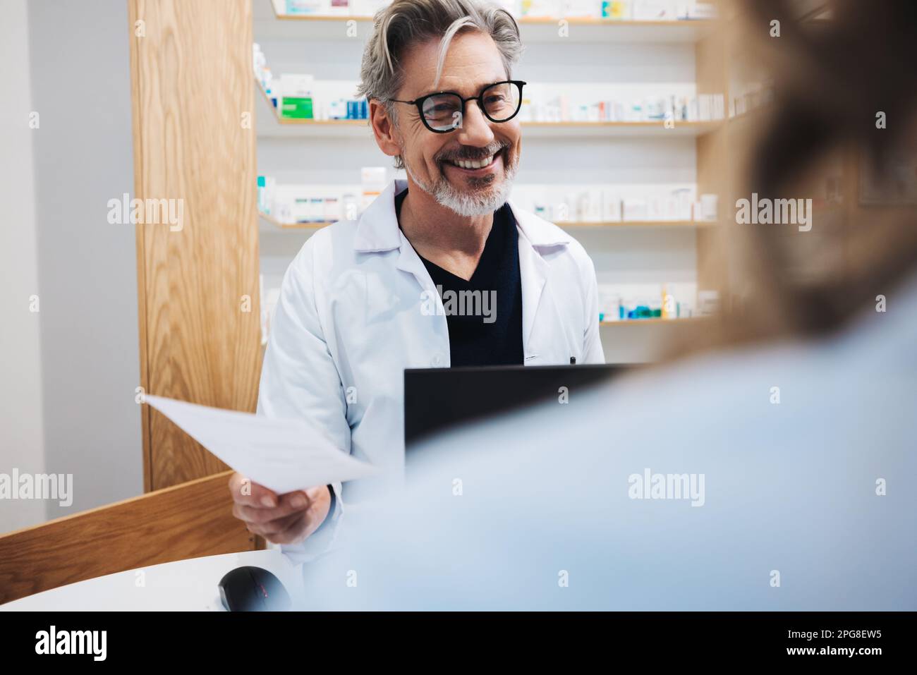 Chefapotheker, der einem Patienten in der Apotheke assistiert. Glücklicher Arzt, der ein Rezept in einer Apotheke ausgibt. Stockfoto