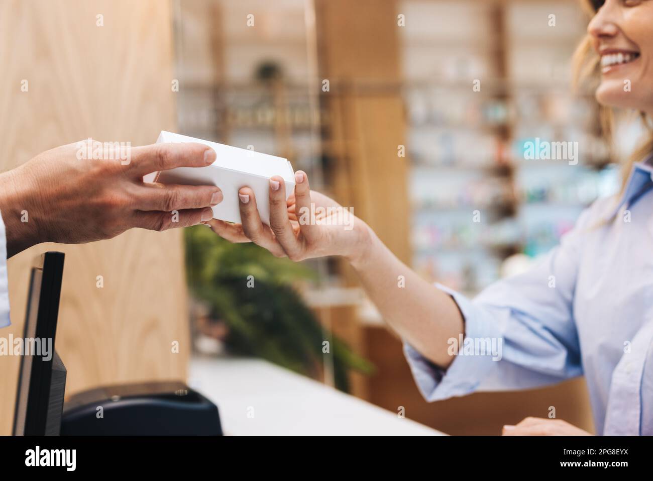Apotheker, der einem Patienten eine Schachtel Pillen in einer Apotheke überreicht. Medizinisches Fachpersonal, das Medikamente über den Ladentisch in einer Apotheke abgibt. Stockfoto