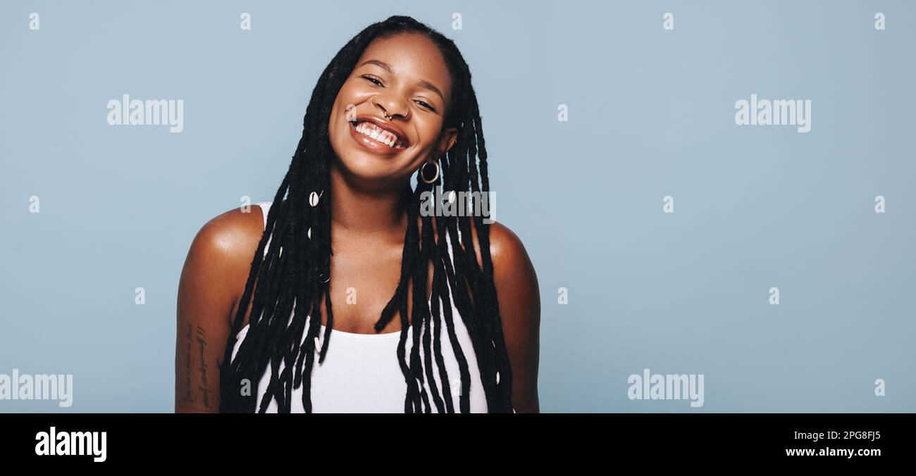 Porträt einer afrikanerin mit Dreadlocks und Piercings, die fröhlich in die Kamera lächelt. Fröhliche junge Frau, die sich selbstbewusst in ihrem Stil fühlt. Fas Stockfoto