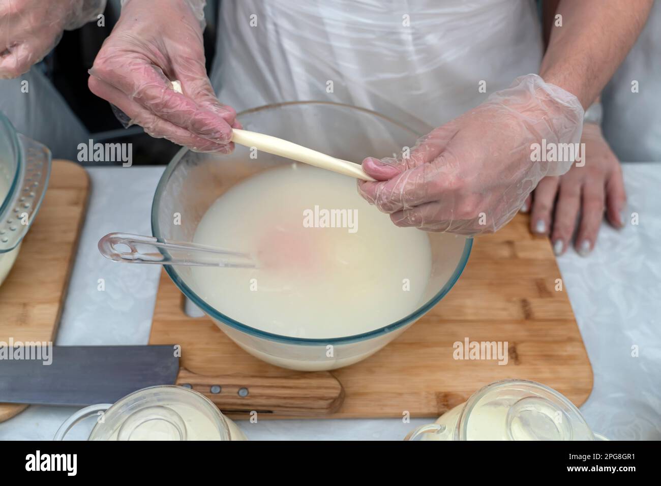 Der Prozess der Herstellung von Käse mit einem Zopf. Hände kneten Käse in Milch. Stockfoto