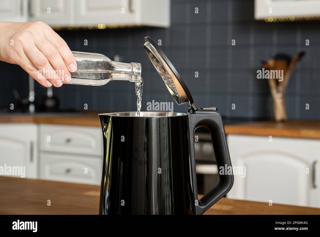 Frau gießt natürlichen destillierten sauren Weißessig in einen elektrischen Wasserkocher, um kochenden Kalk zu entfernen. Entkalken eines Wasserkochers, Entfernen von Kalkablagerungen. Stockfoto