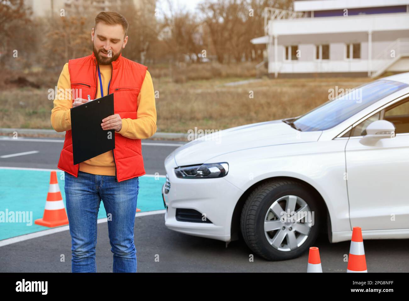 Kursleiter mit Klemmbrett in der Nähe des Fahrzeugs auf der Teststrecke. Fahrschule Stockfoto