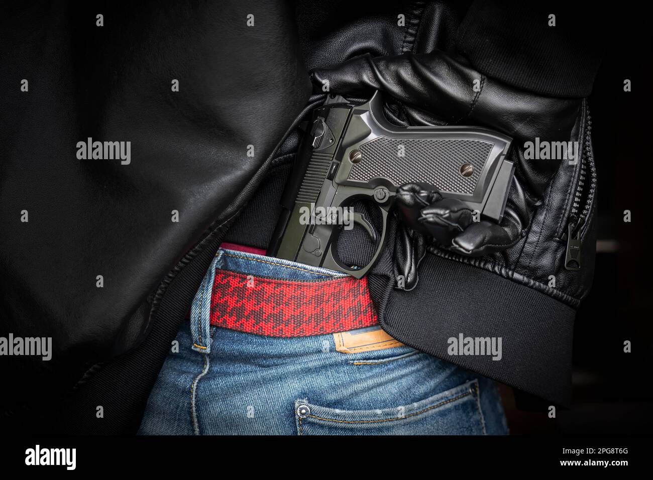 Ein Mann, Polizist oder Räuber, ein Gangster, der seine Waffe hinter seinem Rücken versteckt. Der Schütze zieht eine Waffe unter einer schwarzen Lederjacke heraus. Stockfoto