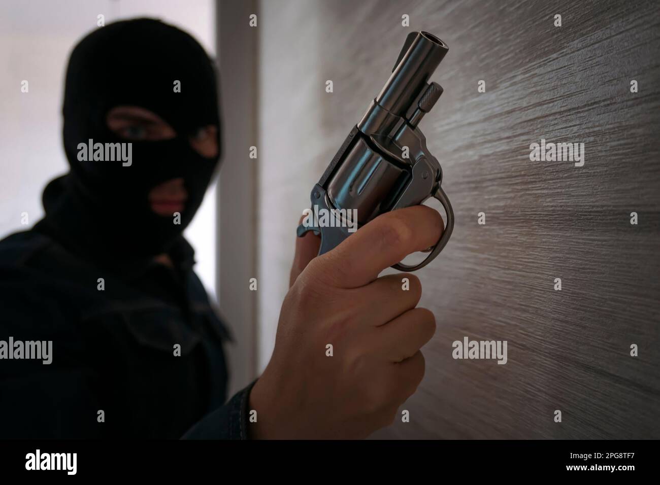 Terrorist in Balaklava, mit einer Waffe in der Hand. Ein Mann, der mit einer Pistole zielt, ein dunkles Gebäude, ein Killer, ein bewaffneter Raubüberfall. Stockfoto