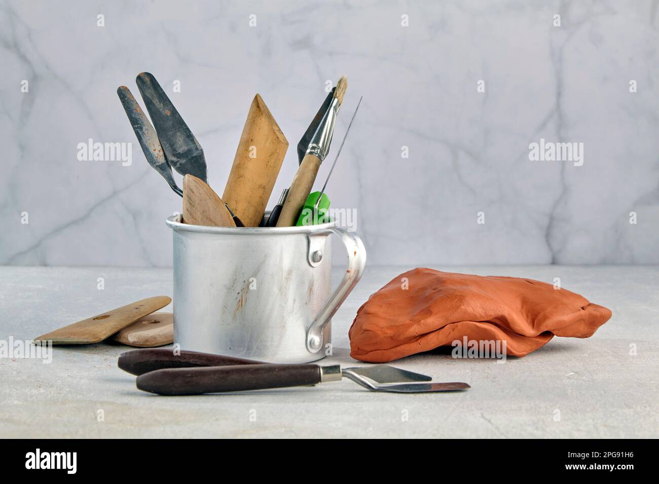 Formen und Modellieren von Werkzeugen in einem Aluminiumbecher und einem Stück Plastik oder Ton auf einem leichten Werkstatthintergrund mit Kopierbereich Stockfoto