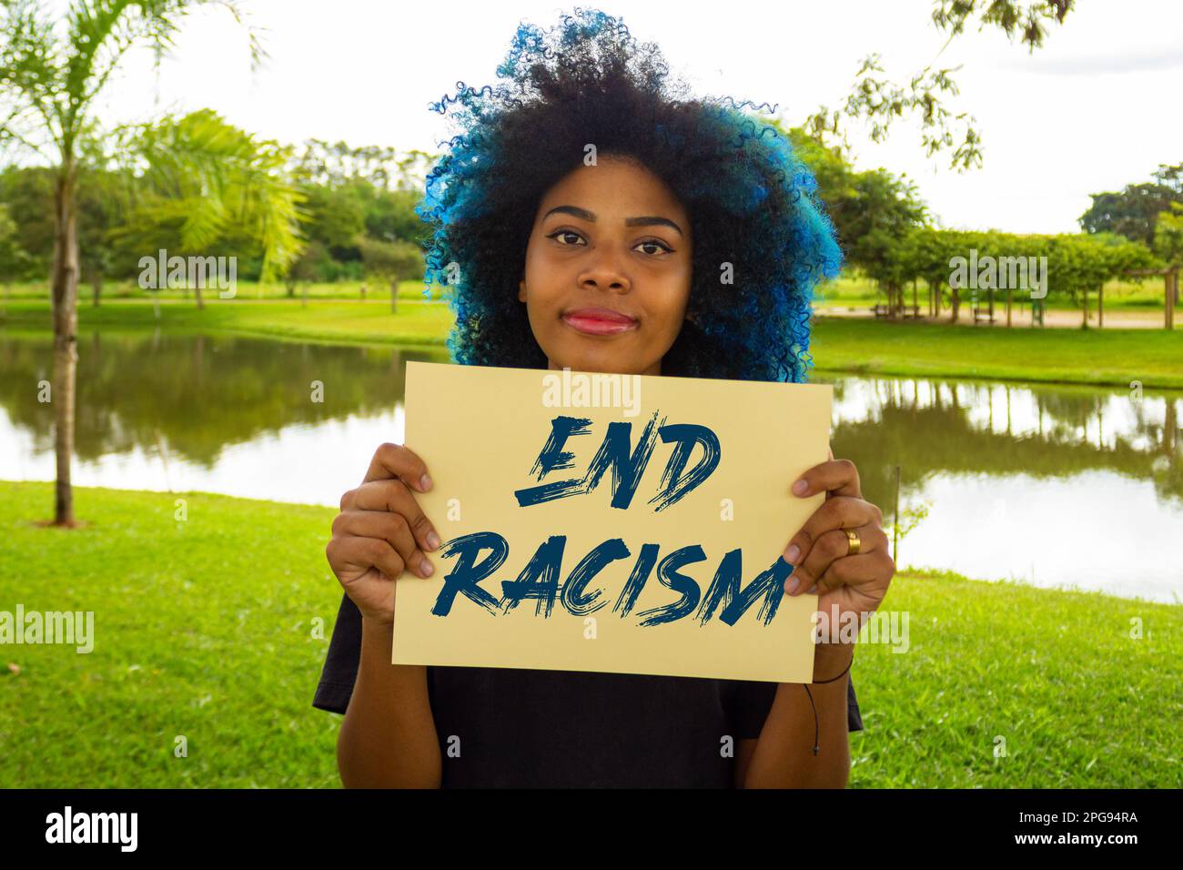 Goiania, Goias, Brasilien – 21. März 2023: Eine junge Frau mit gefärbtem blauem Haar, die ein Schild mit dem Text "Ende des Rassismus" in der Hand hält. Stockfoto