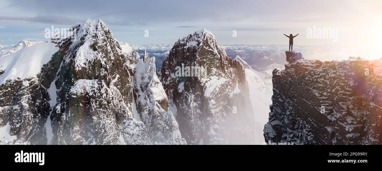 Abenteuerliche Wandererin, die auf einem eisigen Gipfel mit felsigen Bergen im Hintergrund steht. Stockfoto