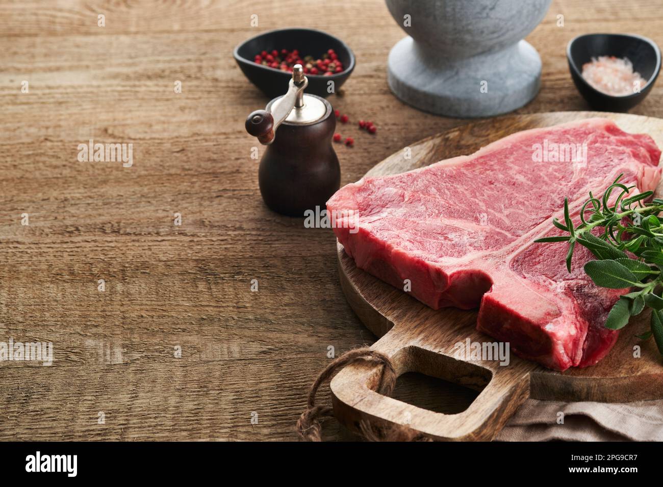 Dickes rohes T-Bone Steak. Trocken gereiftes rohes T-Bone- oder Porterhouse-Rindfleisch-Steak mit Kräutern und Salz auf dunklem Hintergrund. Selektiver Fokus und Kopierbereich. Stockfoto