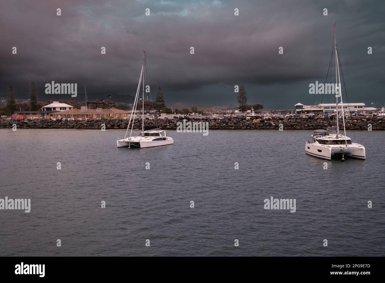 Einige Boote sind an einer Anlegestelle in einem Gewässer mit einem dunklen und vorhersehbaren Himmel im Hintergrund gefesselt Stockfoto