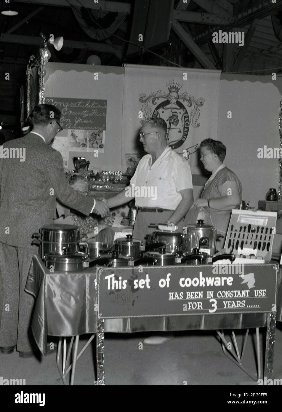 1956, historisch, auf einem Ausstellungsstand für die Anbieter von Kochgeschirr Saladmaster der Lane County Fair, Eugene; Oregon, USA. Besteck aus Edelstahl ist ausgestellt. Banner sagt: „Sein Kochgeschirr wird seit 3 Jahren ständig verwendet.“ Das Unternehmen begann 1947 mit einem Produkt – der Saladmaster Machine – und erweiterte sein Sortiment an Kochgeschirr, um in den 1970er Jahren eines der 100 führenden Unternehmen in Texas zu werden. Stockfoto