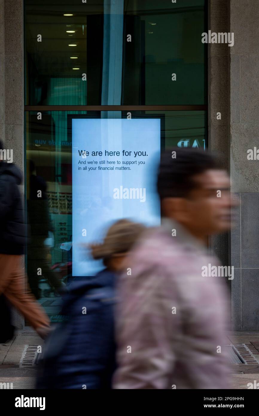 Schilder in den Fenstern der Hauptniederlassung der Credit Suisse in Genf zeigen die Meldung „Wir sind für Sie da“ an. Die Bank, die von ihrer konkurrierenden UBS übernommen wurde, um einen kaskadierenden Bankausfall zu verhindern, versucht nun, ihre Kunden zu beruhigen, die sich um ihr Geld sorgen. Stockfoto