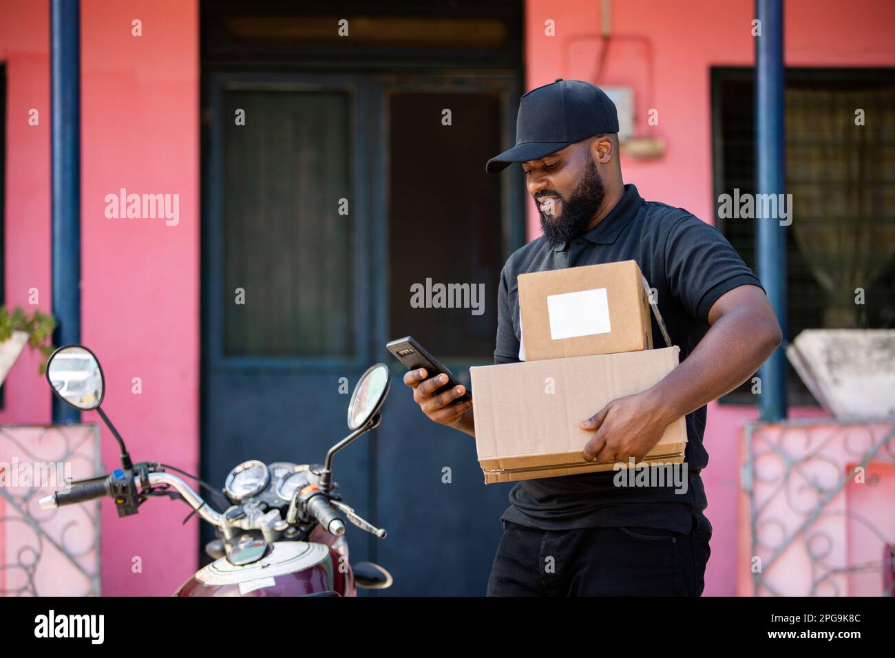 African Delivery Kurier man von Local Postal Shipping Service liefert Postpakete mit Motorrad in African Home. Stockfoto