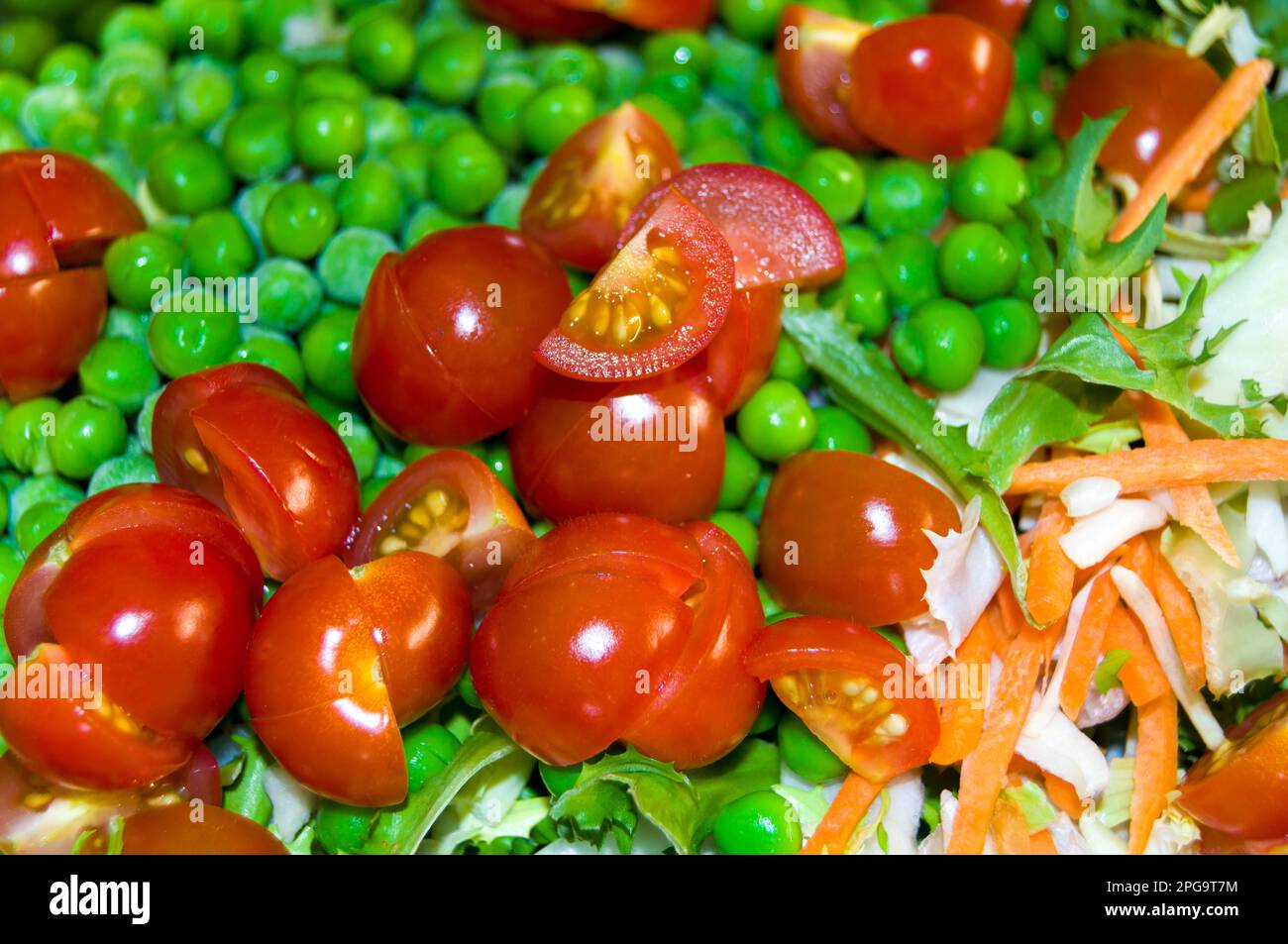 Salat aus in Scheiben geschnittenen Kirschtomaten, gefrorenen Erbsen, geriebener Karotte und Eisbergsalat. Stockfoto