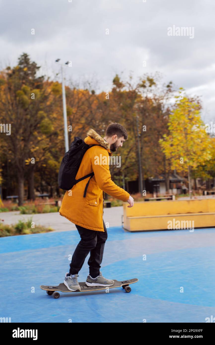 Ein eleganter, lässiger junger Mann in voller Höhe, der sich im Skatepark bewegt, mit Bart, Seitenansicht Stockfoto